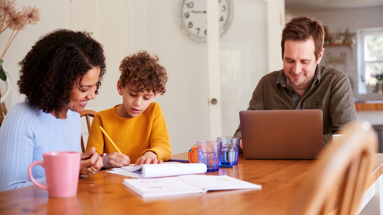 A family is working on a laptop while sitting at a table.