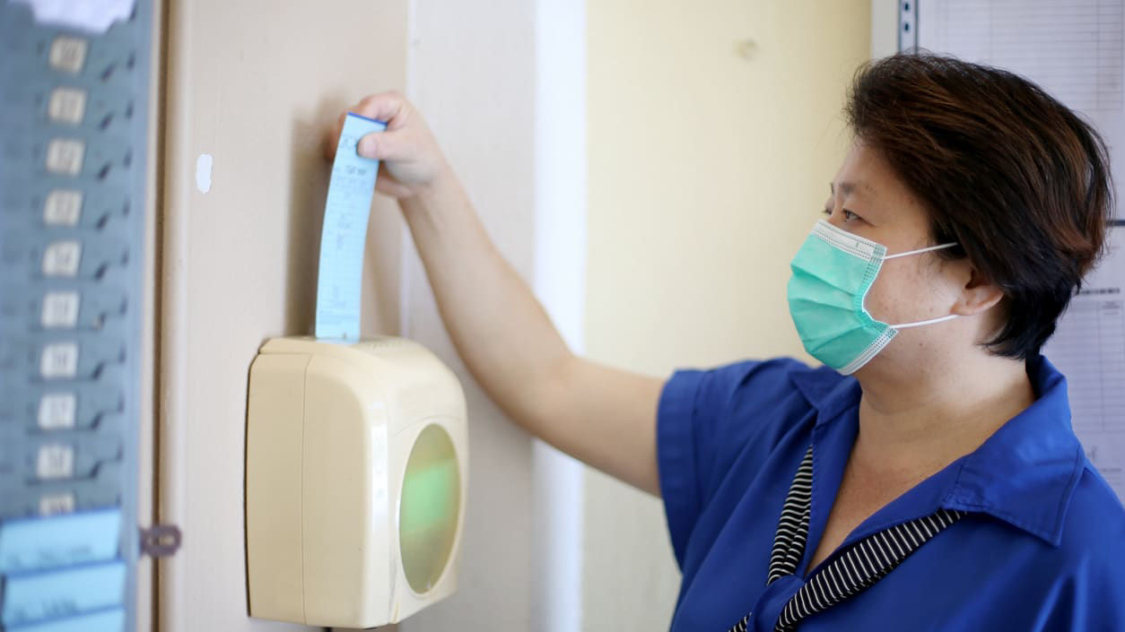 A woman wearing a surgical mask is putting on a face mask.