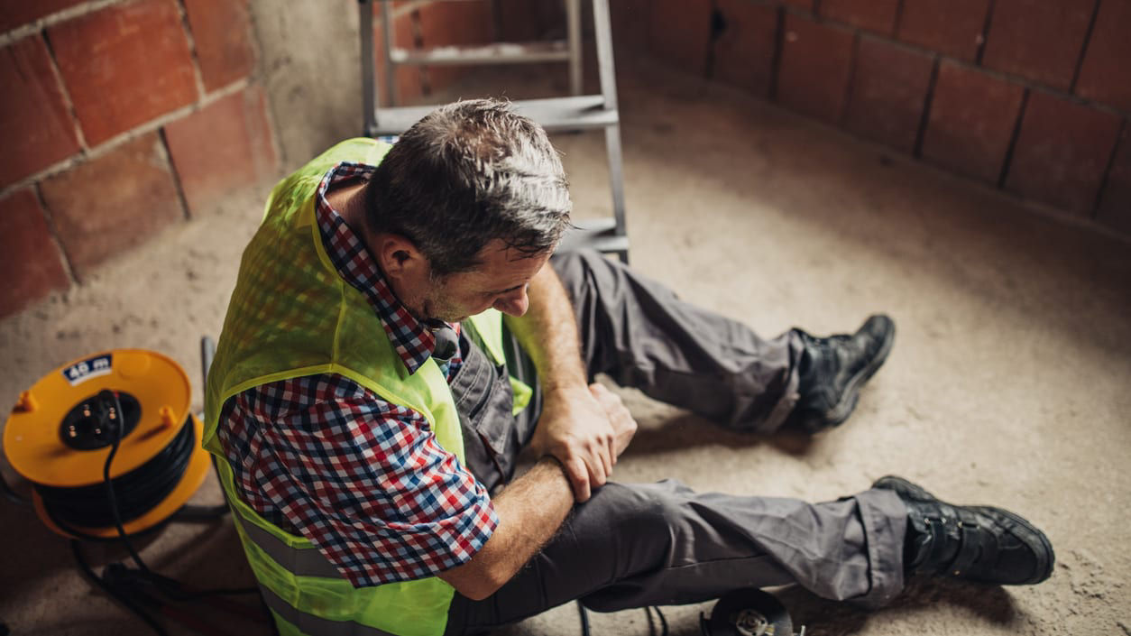 A construction worker sitting on the floor with a ladder.