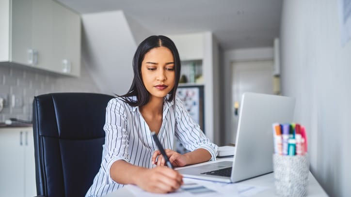 A woman sitting at a desk with a laptop and a pen.