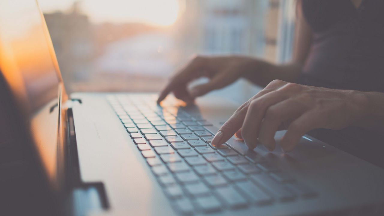 A woman typing on a laptop in front of a window.