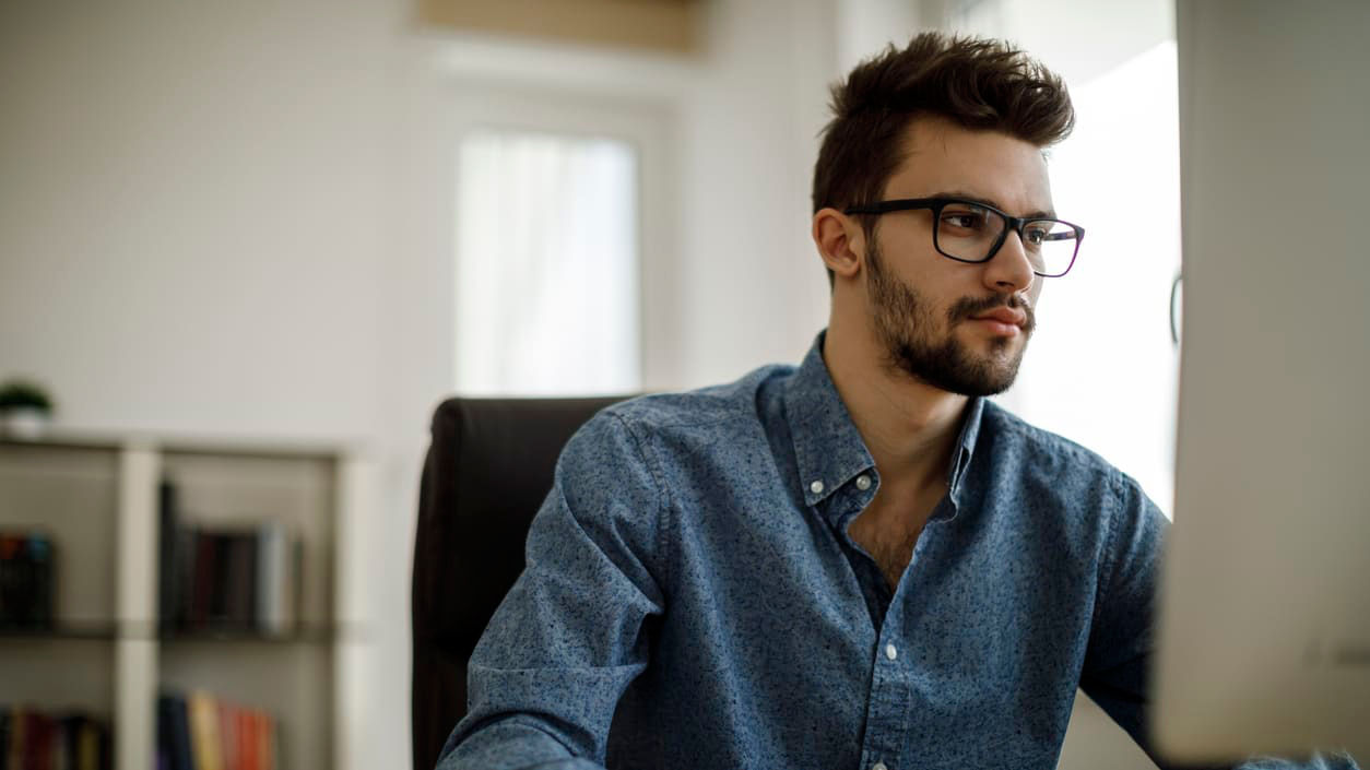 A man wearing glasses is sitting at a desk in front of a computer.