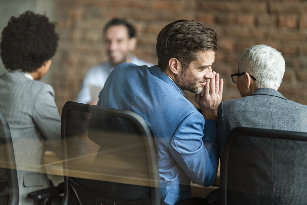 Man whispers to colleague during business meeting