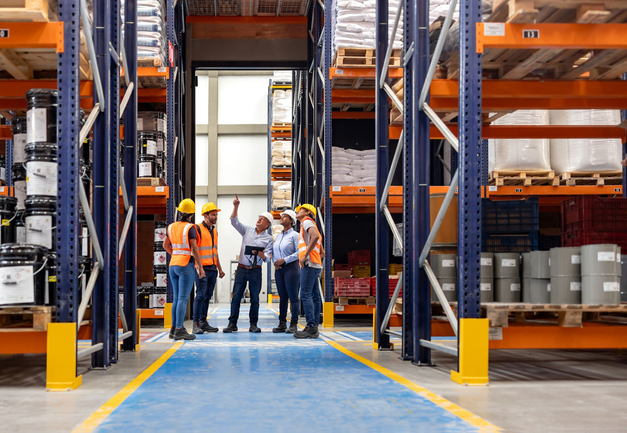 Forperson talking to a group of employees in a meeting at a distribution warehouse and pointing away