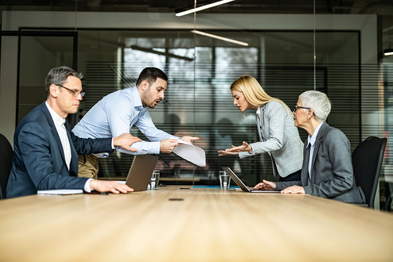 Frustrated colleagues argue about paperwork during a meeting with their coworkers in the office.