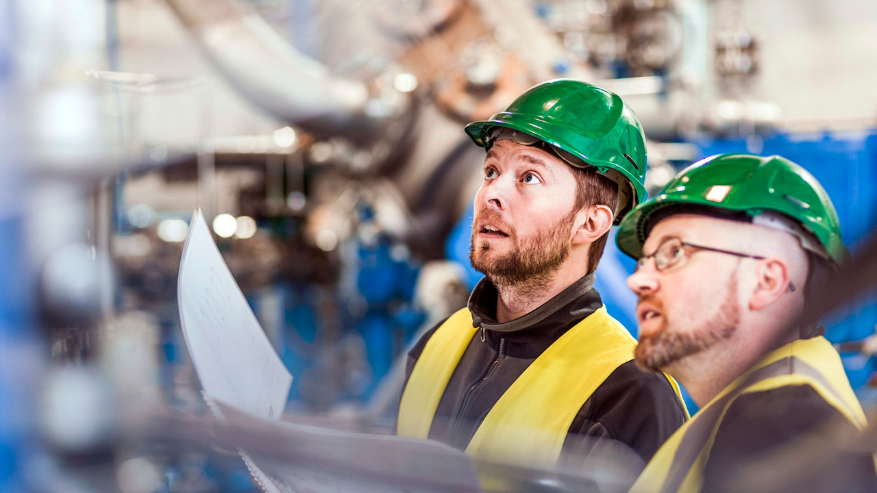 Two men in hard hats looking at paper in a factory.