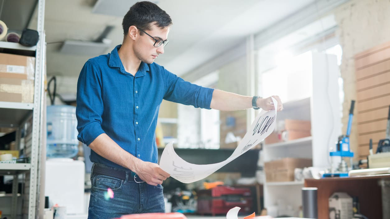 A man is looking at a sheet of paper in a workshop.