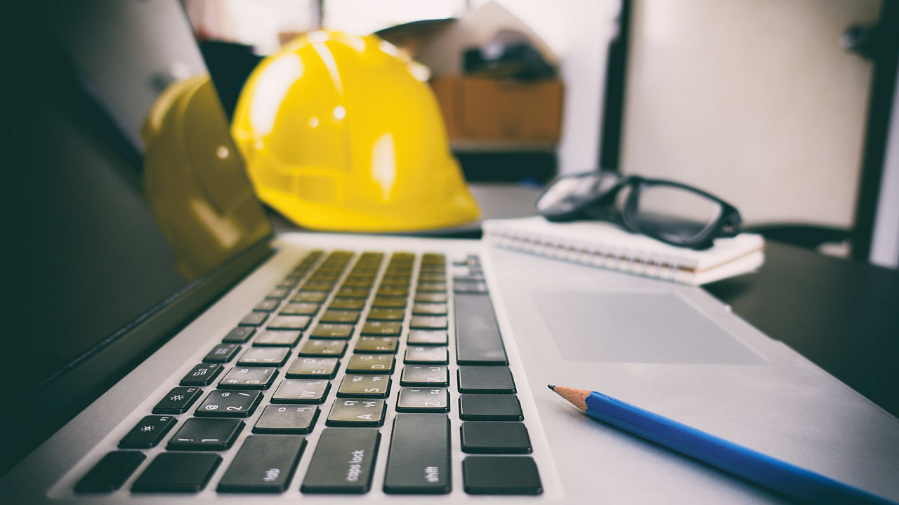A laptop with a hard hat and a pencil on it.