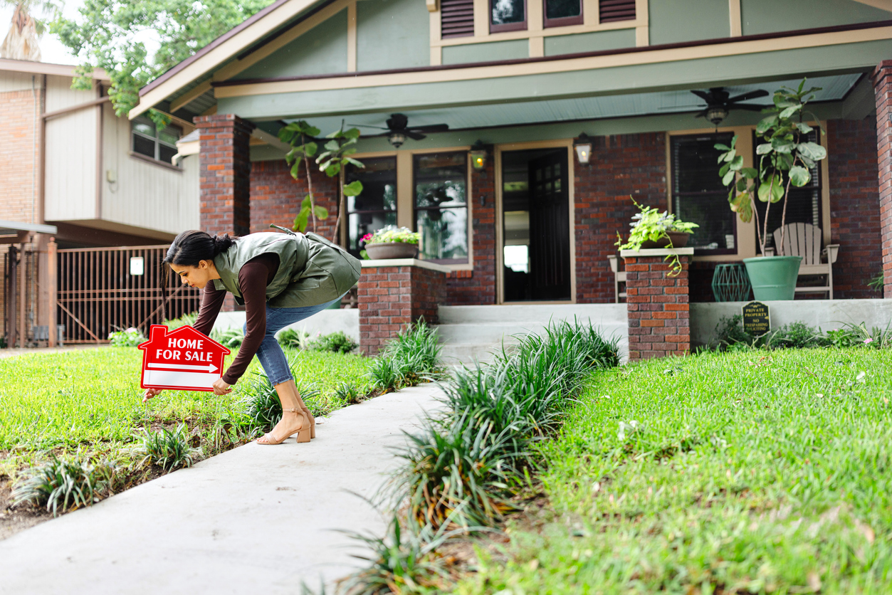 person putting out "for sale" sign in front of a house