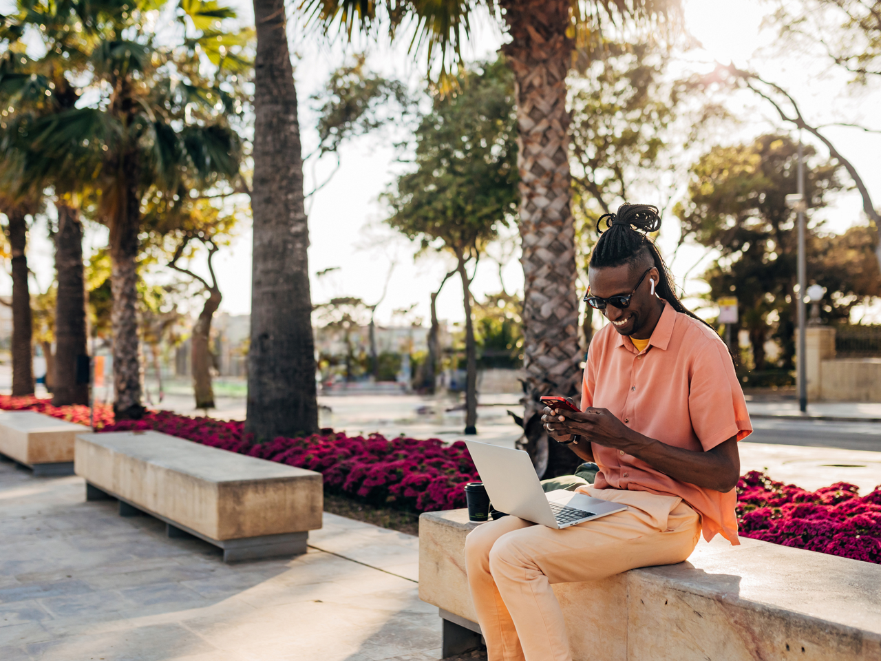 man works from his phone and laptop at a park in california