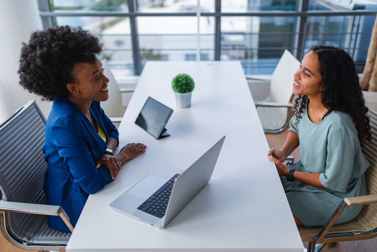 An attractive black female financial consultant smiling during a  meeting with a client at her office. She looks happy and professional while having a conversation with her client. Both females look relaxed and content.