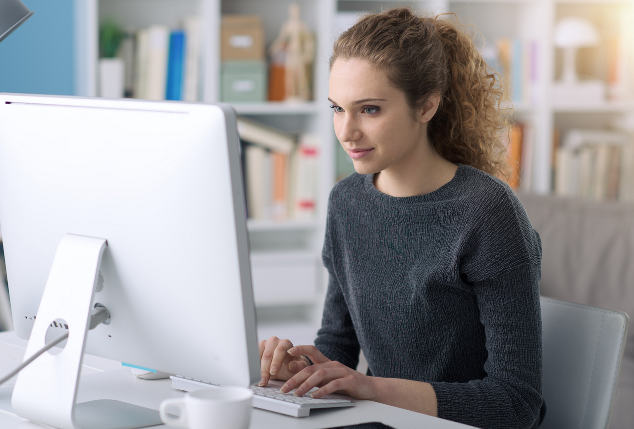 Young beautiful woman using a computer in the office and connecting online, she is typing and chatting