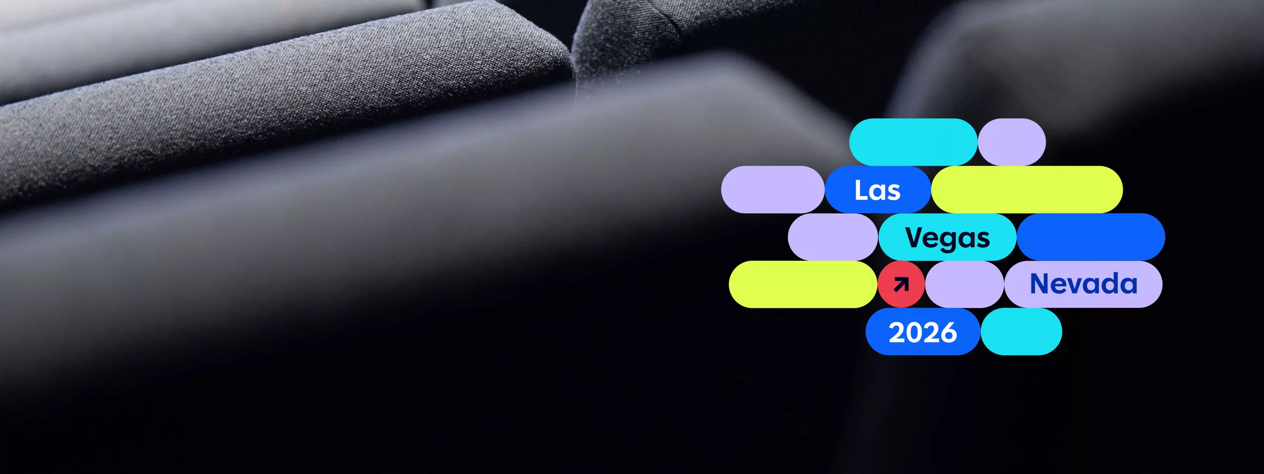 A close-up view of dark upholstered theater or auditorium seats is shown. On the right side, a colorful graphic overlay displays the words 'Las Vegas Nevada 2026' in bold, modern typography. The image combines a sleek, professional setting with vibrant, playful design elements, suggesting an upcoming event or conference. The number '2026' is clearly visible in the graphic.