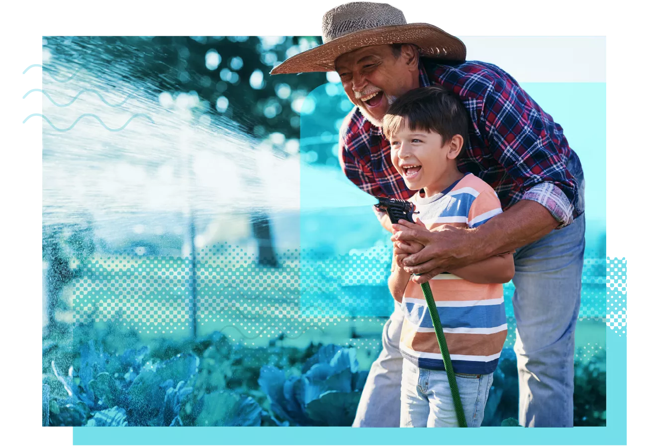 father and son laughing while spraying water from a hose