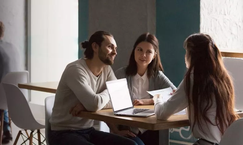 Group of three  people sitting around a table with laptop open