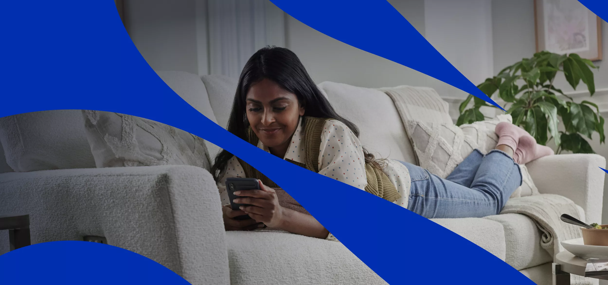 A young woman lies comfortably on a light-colored sofa while looking at her smartphone. She appears to be in a cozy living room with soft cushions and a side table nearby. Blue abstract graphic shapes overlay the image, adding a modern, dynamic visual style. The overall scene suggests relaxation, casual browsing, or staying connected at home.