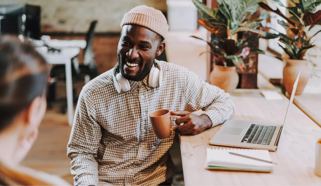Man in front of computer laughing and holding coffee cup
