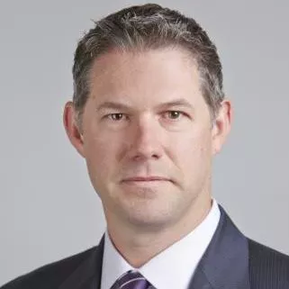 Formal headshot of a professionally dressed man in a suit and tie. He faces the camera with a neutral expression against a plain light gray background. The image emphasizes his face, upper shoulders, and business attire. The overall style is clean, corporate, and suitable for professional profiles or corporate communications.