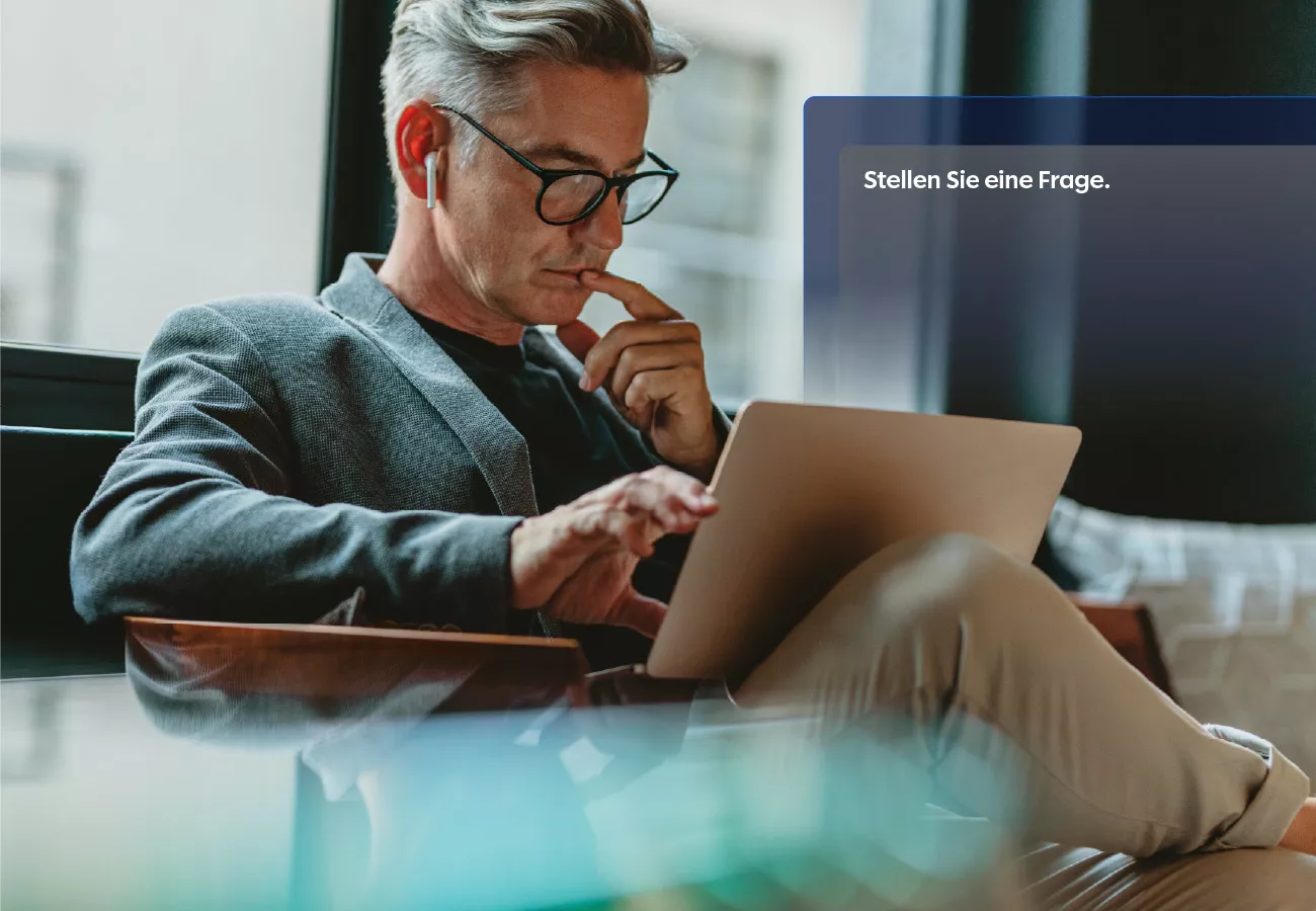 A mature adult sits comfortably in a contemporary office setting, focused on a tablet device. The individual is dressed in business attire and appears to be engaged in thoughtful work or communication. The environment features large windows and a relaxed, professional atmosphere. The visible text on the screen reads 'Stellen Sie eine Frage.'