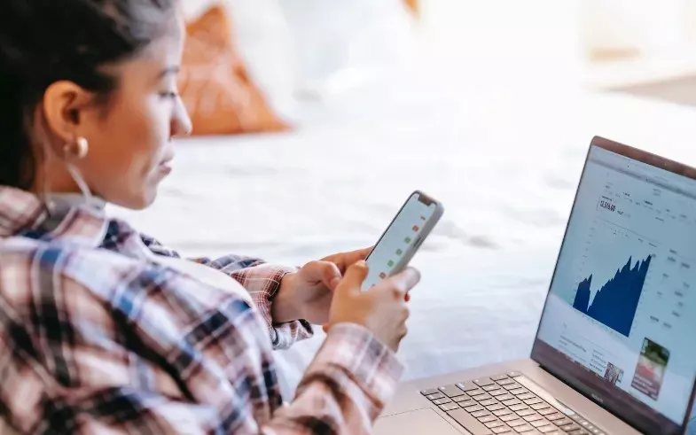 Person on cell phone while looking at chart on laptop