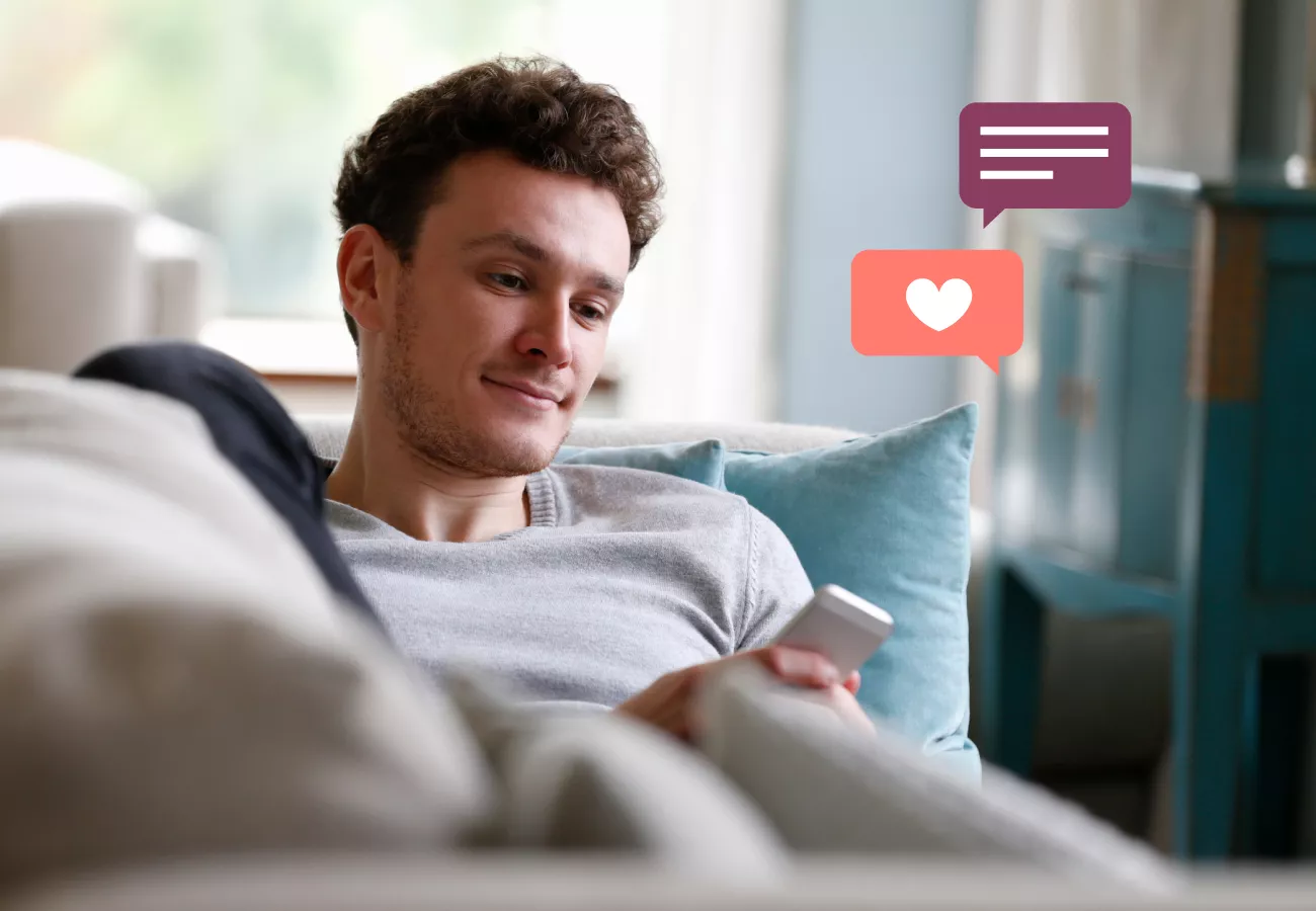 man laying on a couch smiling while using his phone