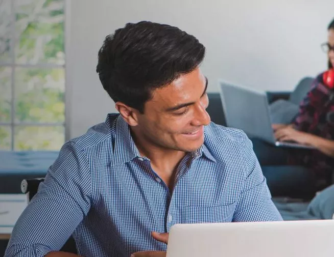 Man looking down toward laptop on table and smiling at person next to him