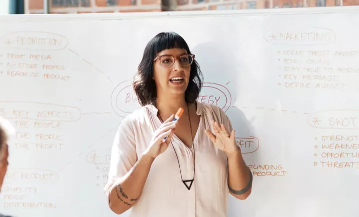 Woman standing in front of a whiteboard with marker in hand and talking