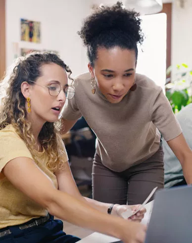 Two women working in an office at a computer discussing a project.