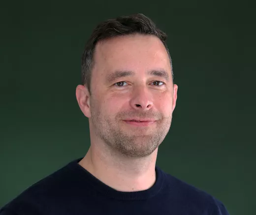 Paul Ribka, Director AI Transformation, vor einem grünen Hintergrund.