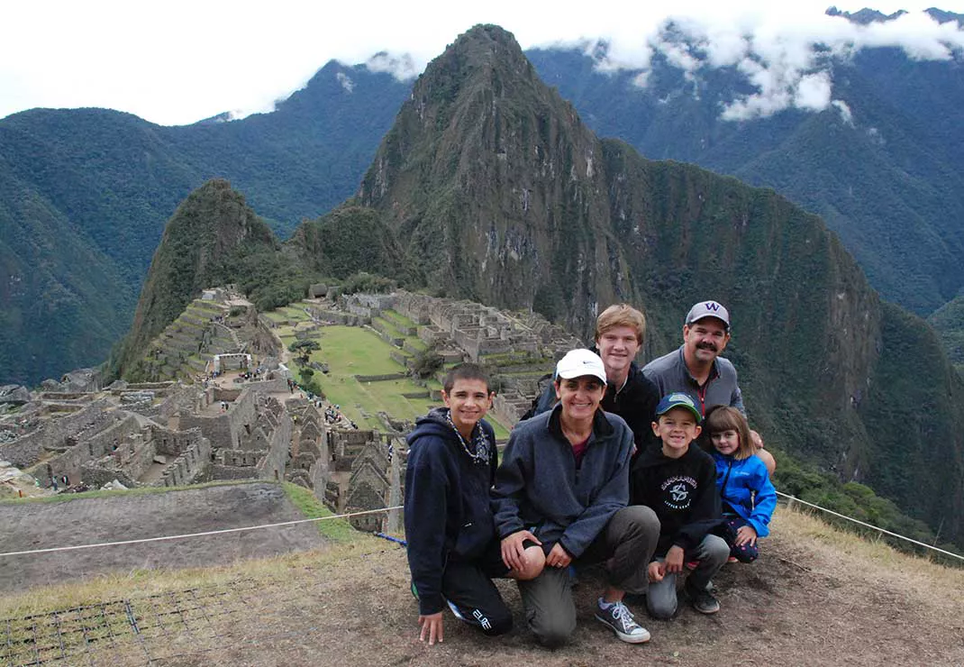 Seattle general manager Jila Javdani wearing white hat and dark clothes, crouched in front of Machu Picchu in Peru with her husband, three sons, and young daughter.