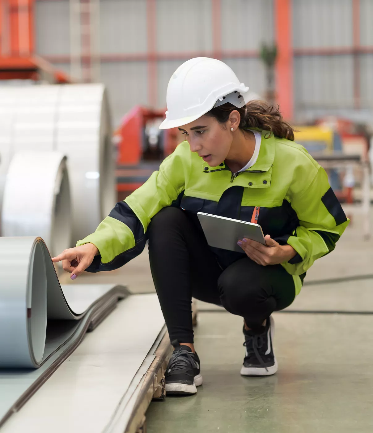 Metalwork manufacturing, warehouse of raw materials. Female factory worker inspecting quality rolls of metal sheet in factory during manufacturing process, wearing safety uniform, use digital tablet