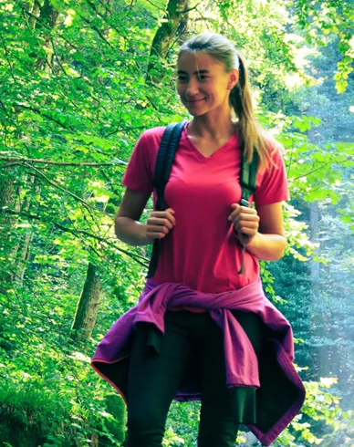 Woman hiking in pink shirt with backpack and jacket tied around waist