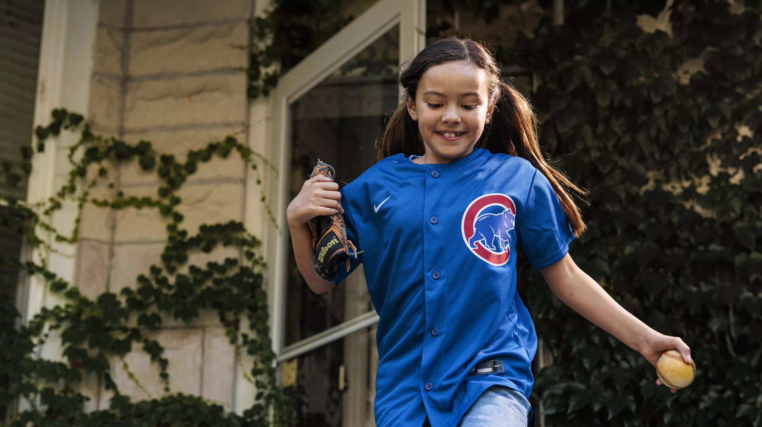 Ein junges Mädchen mit Baseballtrikot läuft nach draußen, um Baseball zu spielen.