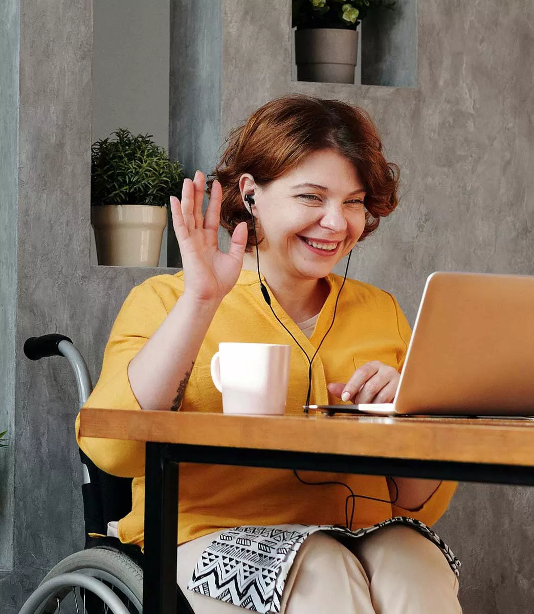 Woman working on laptop waving with headphones