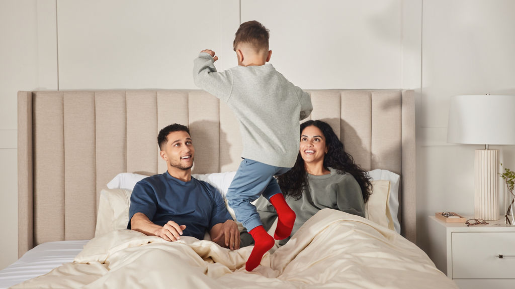 Woman laying on bed in grippy socks holding a hot beverage and wearing a funny looking hat.