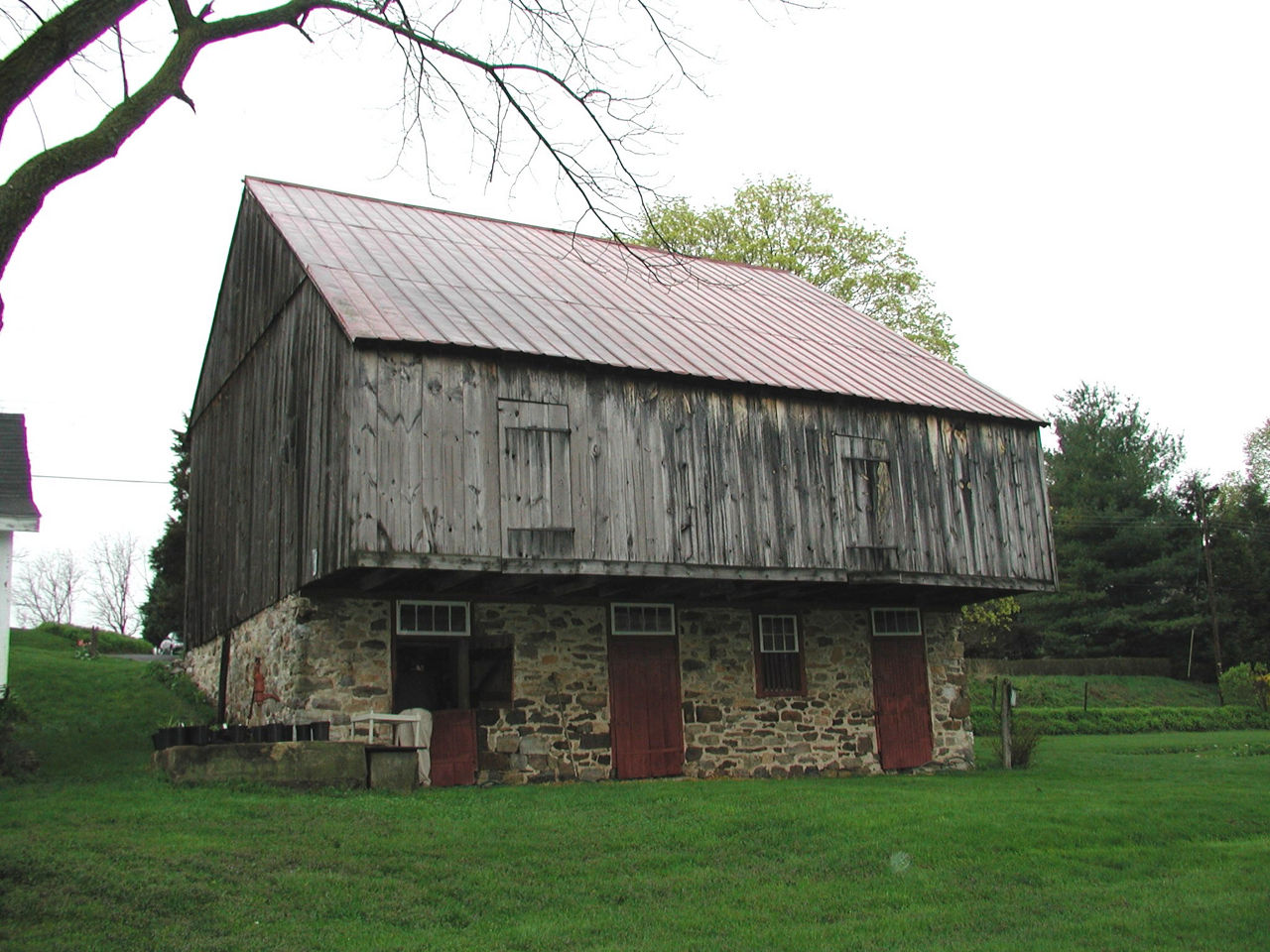 Large two-story wood and stone barn with an overhanging forebay and side gabled roof.