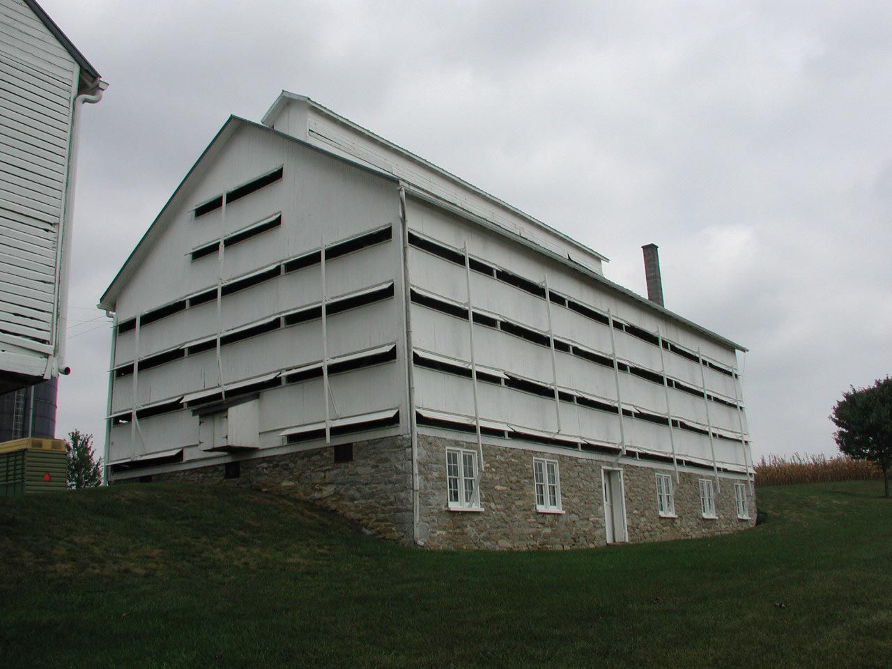Tall and narrow frame barn with horizontal louvered panels and a stone foundation with a roof ventilation clerestory.