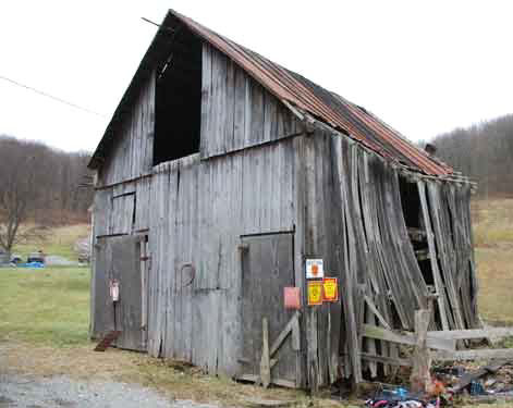 Small unpainted wood barn with a front facing gable roof and hay door under the peak.