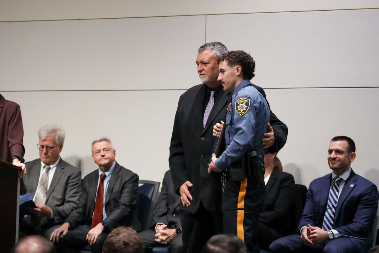 Don Numer, Training Supervisor, stands with Northampton County Deputy Alex Cameron as Cameron receives the Firearms Award during the 72nd Sheriffs’ & Deputy Sheriffs’ Basic Training Academy Commencement Ceremony. The two pose together on stage as seated attendees look on.