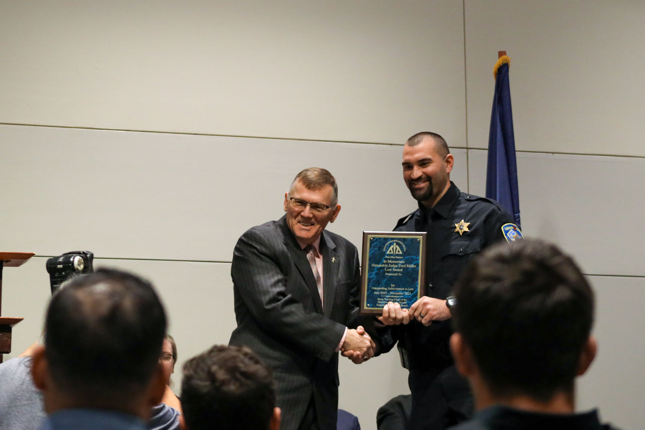 Magisterial District Judge Jerome Nevling presents the Honorable Judge Fred Miller Memorial Law Award to Lebanon County Deputy Anthony Pletz during the 72nd Sheriffs’ & Deputy Sheriffs’ Basic Training Academy Commencement Ceremony. The two shake hands as Deputy Pletz smiles and holds the award plaque.