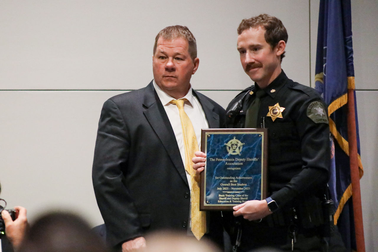 Douglas O. Hummel, Criminal Justice System Specialist II with PCCD’s Bureau of Training Services, stands beside Luzerne County Deputy Ryan Morgans as Morgans holds a plaque recognizing him as the recipient of the Overall Best Student Award during the 72nd Sheriffs’ & Deputy Sheriffs’ Basic Training Academy Commencement Ceremony.