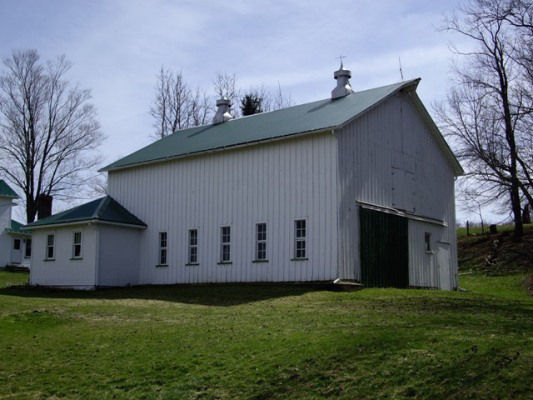Two-story gable front barn with vertical white painted wood siding and narrow sash windows along the side elevation.