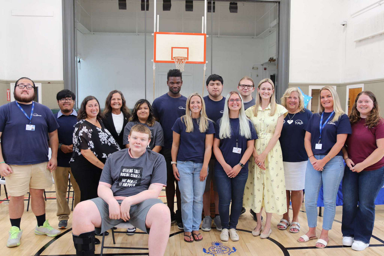 A group of people posing together in a gymnasium, with a basketball hoop in the background.
