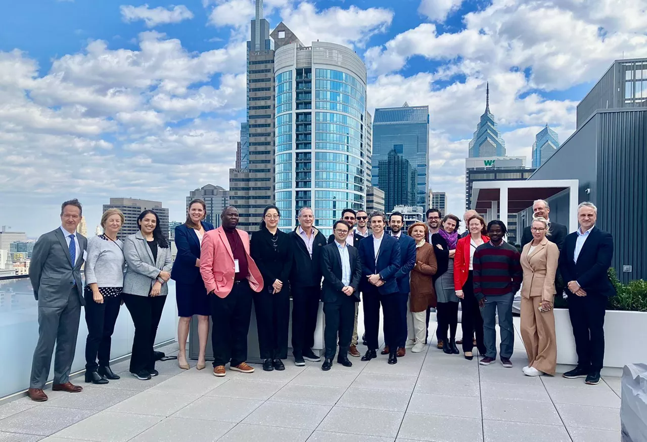 A group of businesspeople pose for a photo in front of the Philadelphia skyline
