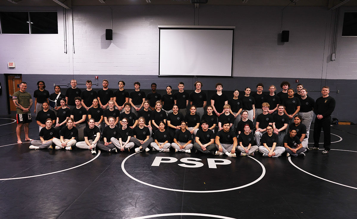 A group of Hill Impact Cadets and instructors pose in a gym