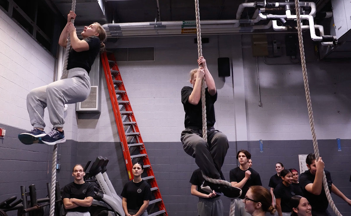 A group of Hill Impact Cadets watch as two cadets climb ropes in a gym