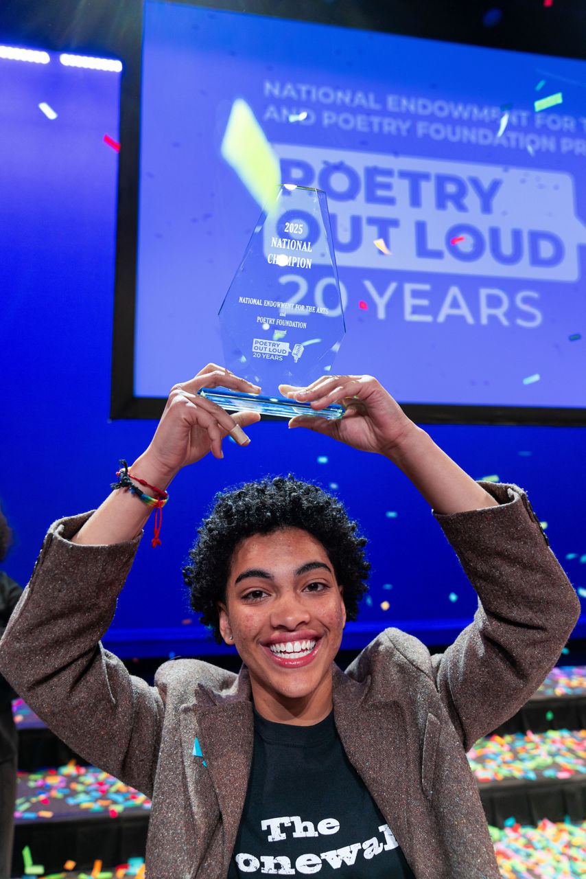 2025 Poetry Out Loud national champion Isavel Mendoza from Pennsylvania poses with trophy above head, while smiling