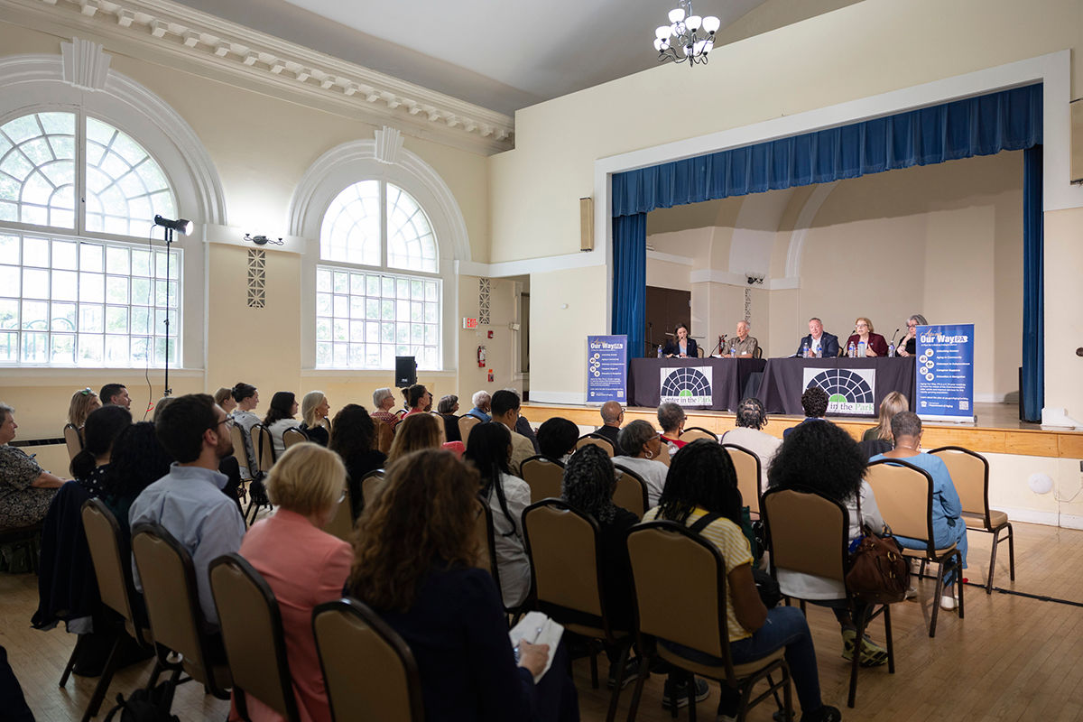 a panel of speakers sits on a stage in a large room in front of a seated audience