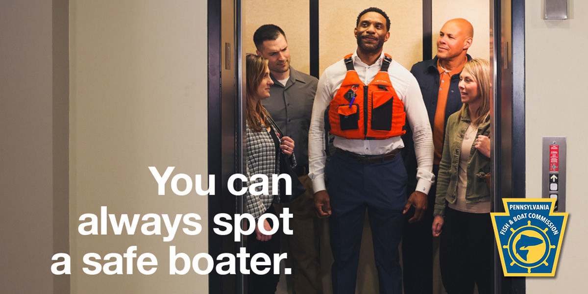Staff at working staring confused at a man wearing a life jacket in an elevator at the office. Text says "You can always spot a safe boater." Pennsylvania Fish and Boat Commission logo in the bottom right corner.