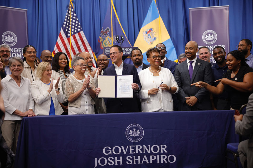 Governor Shapiro holding up a signed bill surrounded by smiling people. 